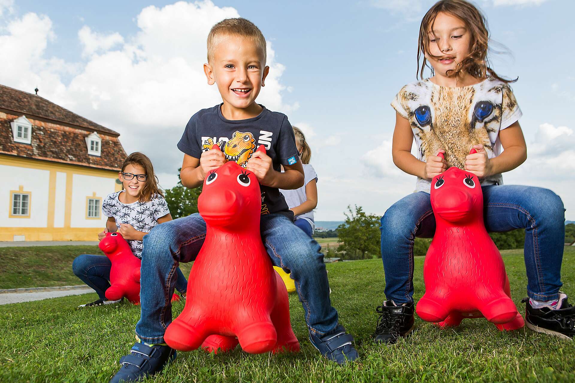 Drei Kinder sitzen auf roten Plastikpferden und reiten über Schloss Hof